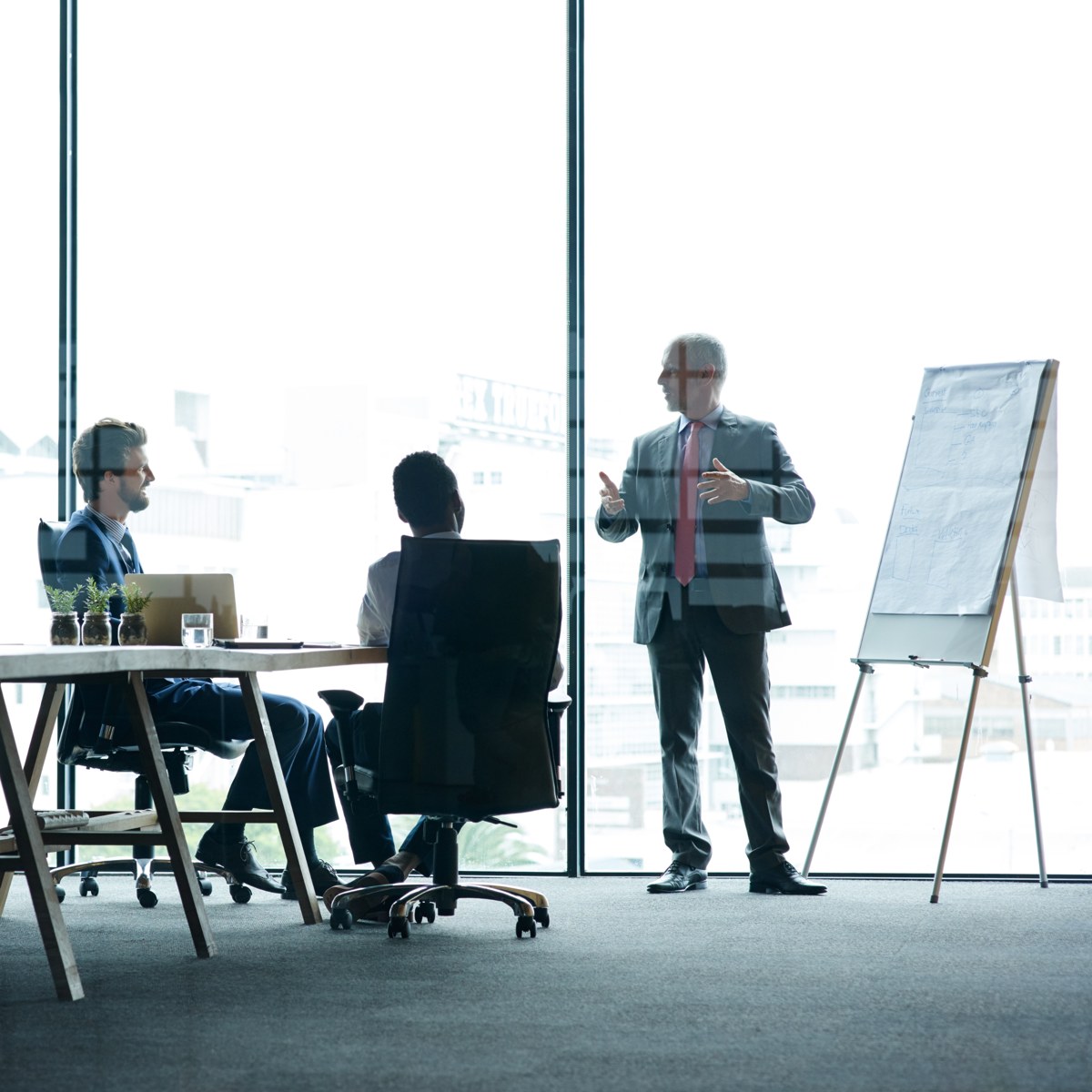 A leader presenting at a flip chart to two colleagues in a modern office